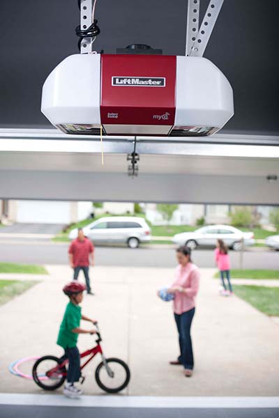 Family enjoying outdoor activities while a LiftMaster garage door opener is visible in the garage above.