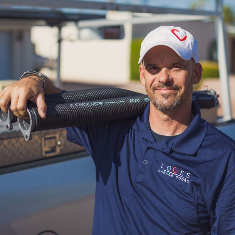 Professional technician from Loves Garage Doors holding springs, ready for installation work outdoors.