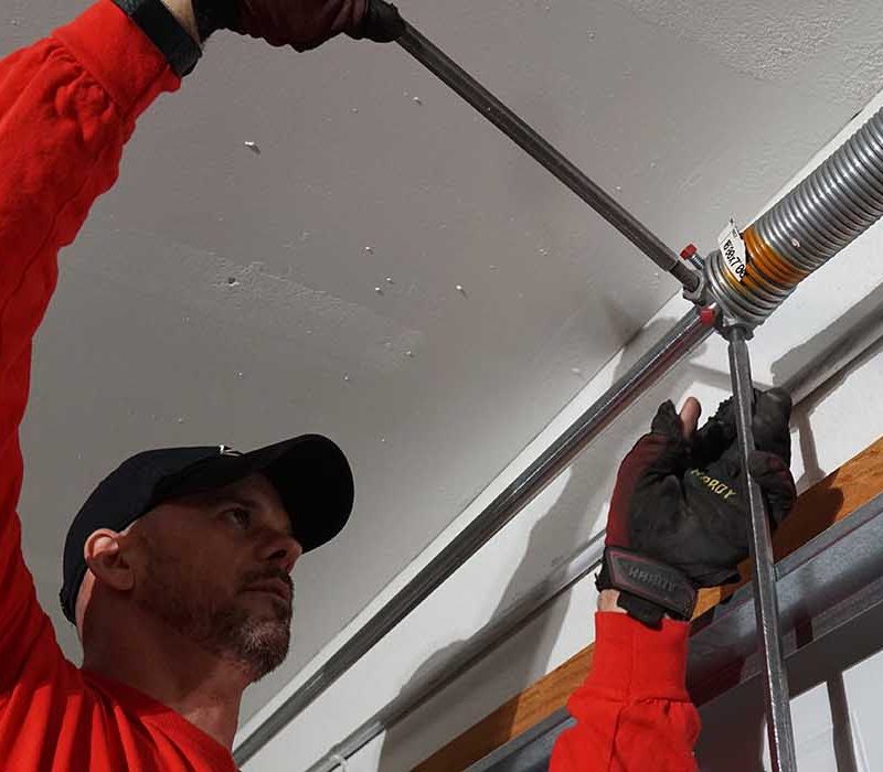 Technician adjusting garage door spring in a residential setting, showcasing repair expertise and safety gear.