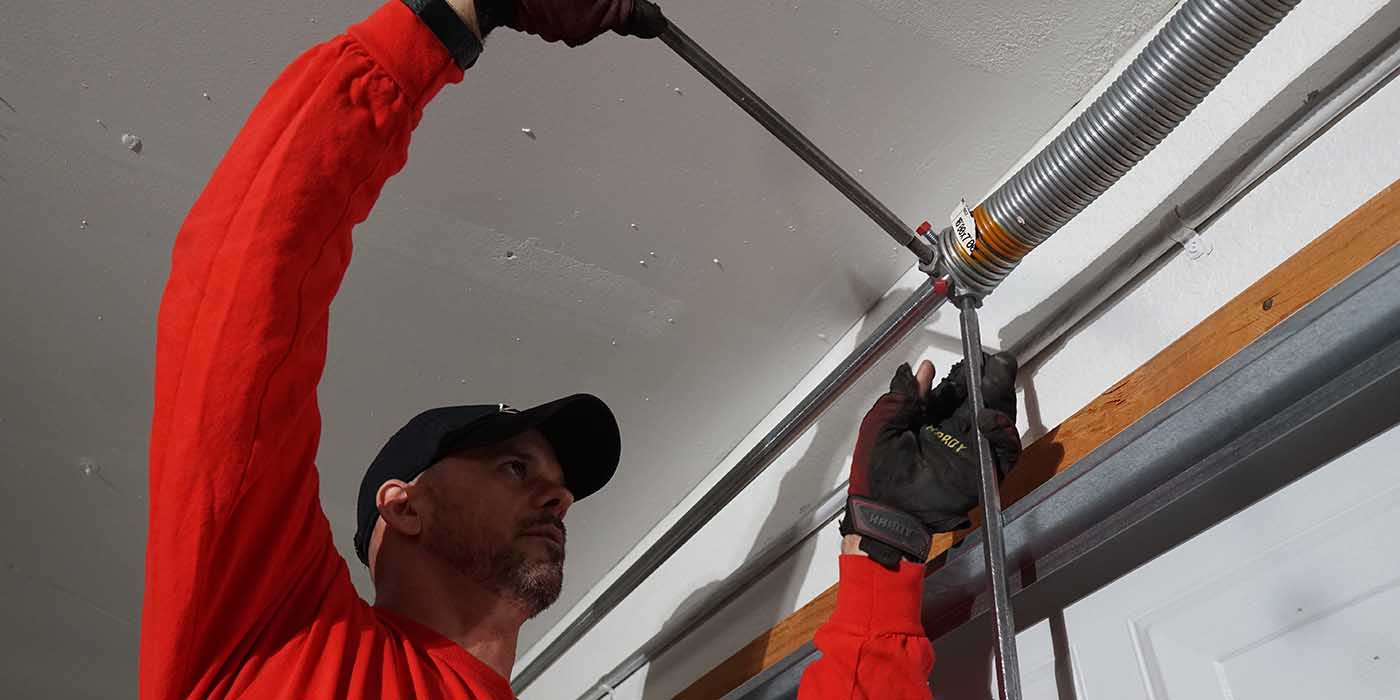 Technician adjusting garage door spring in a residential setting, showcasing repair expertise and safety gear.