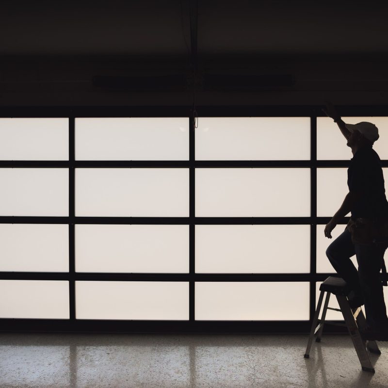Silhouette of a worker on a ladder, reaching towards a garage door during home improvement or maintenance.