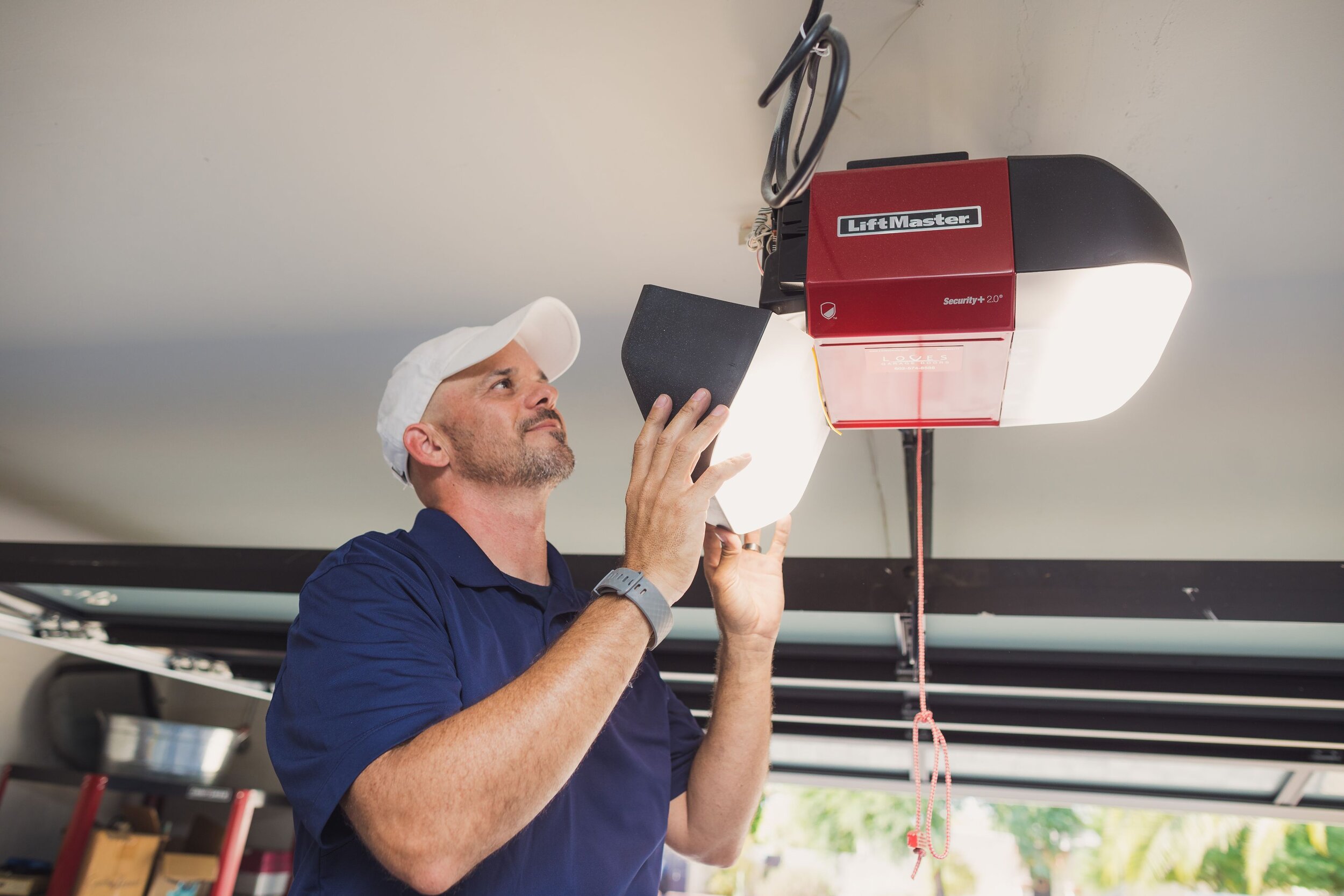Man installing a LiftMaster garage door opener in a well-lit garage, demonstrating home improvement skills.
