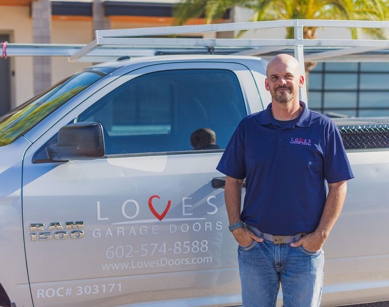 A technician from Love's Garage Doors stands proudly beside a branded service truck, ready to assist customers.
