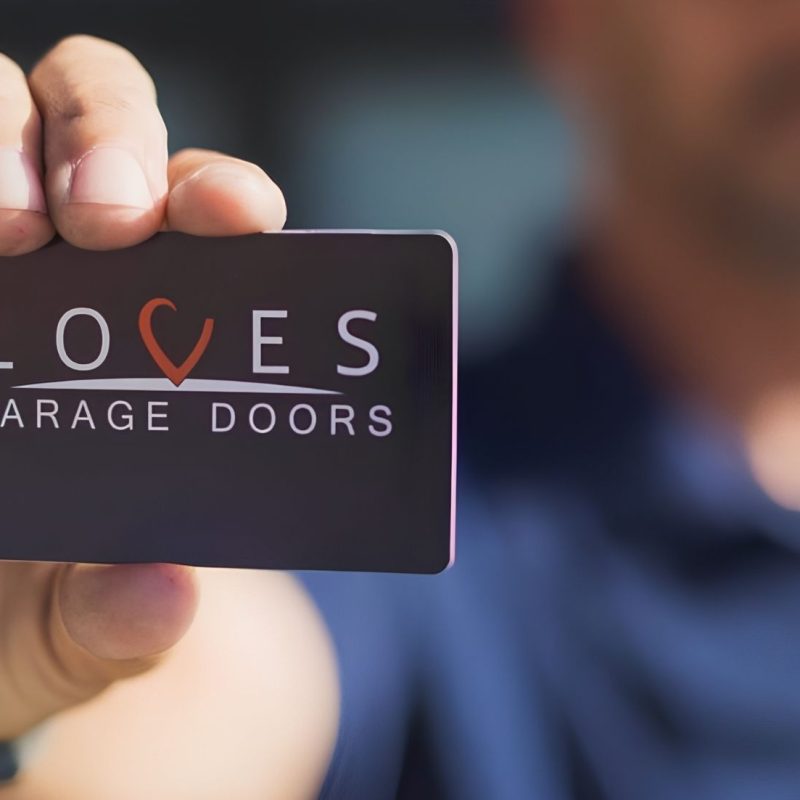 A technician holds a Loves Garage Doors business card, representing professional commercial overhead door services.