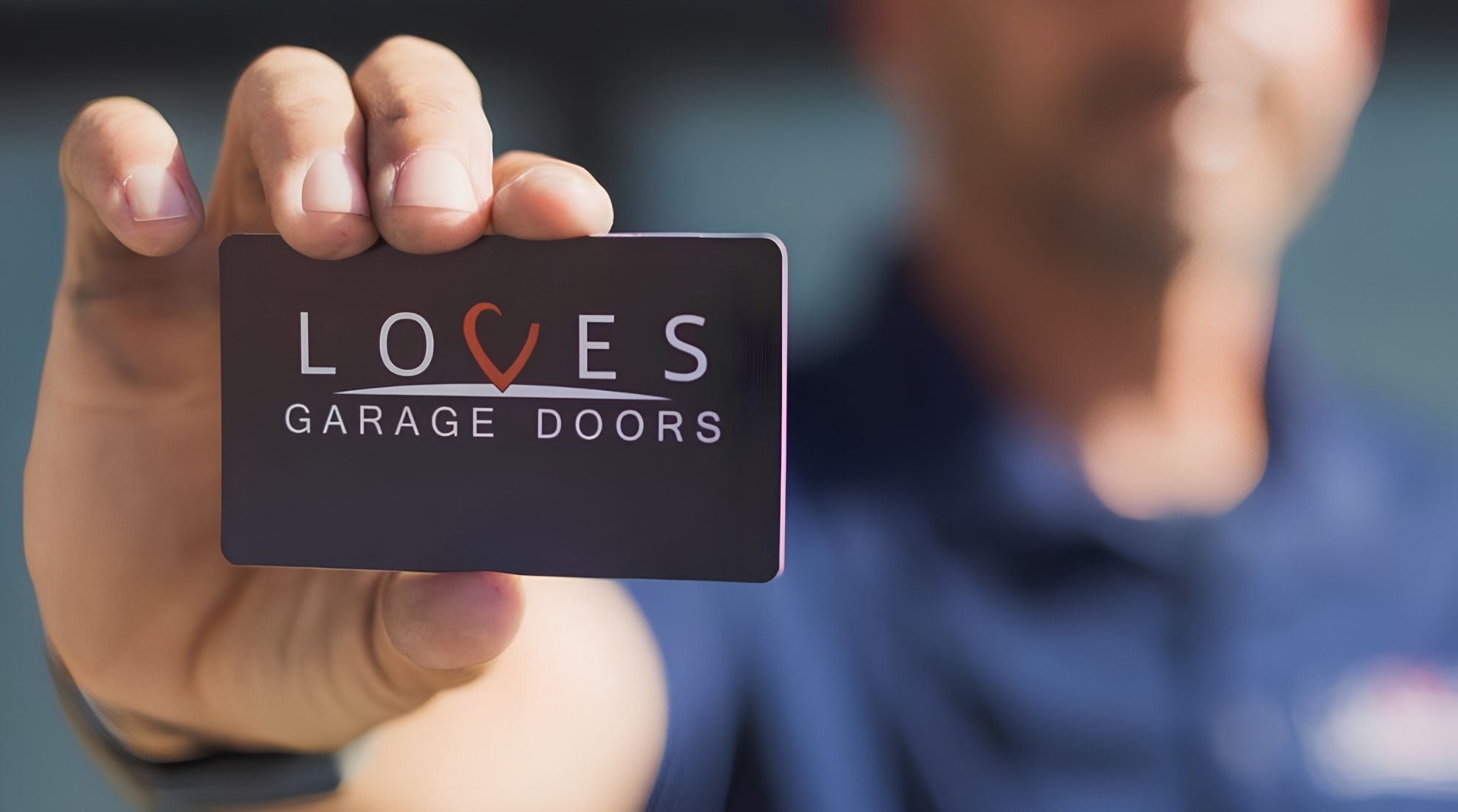 A technician holds a Loves Garage Doors business card, representing professional commercial overhead door services.