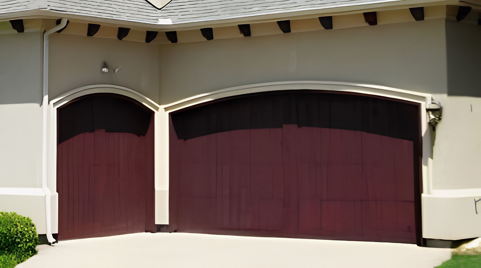 Two well-maintained dark red wooden garage doors on a stucco home, highlighting the benefits of preventive care.
