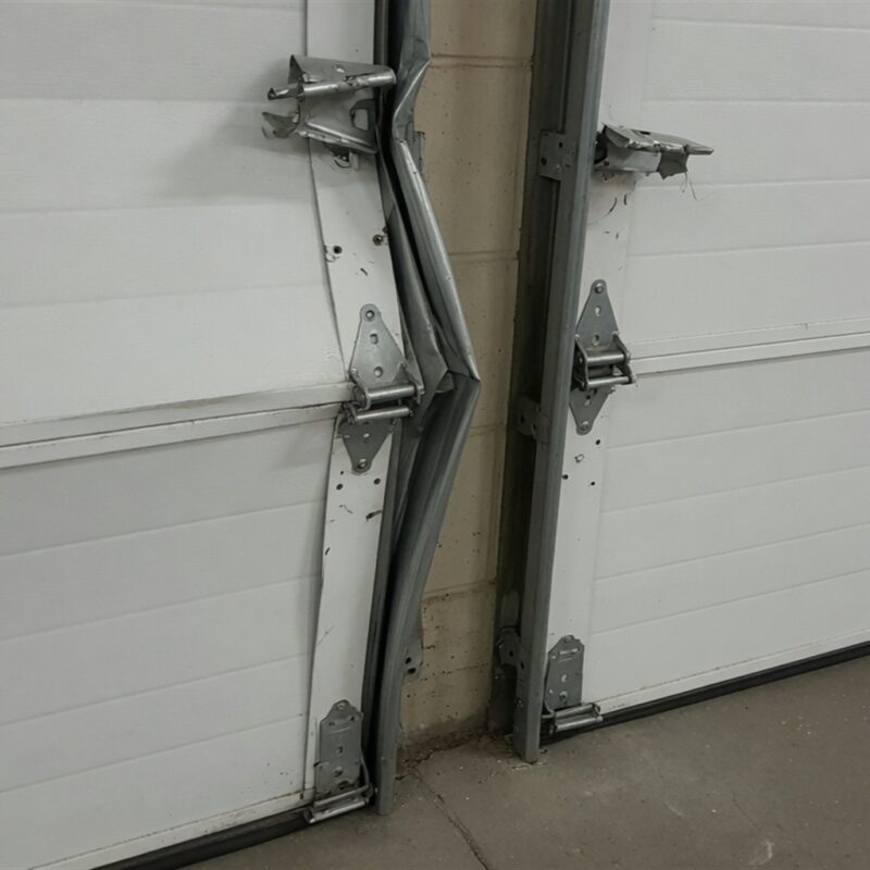 Damaged garage door with misaligned panels and bent track, showcasing the need for repair or replacement.