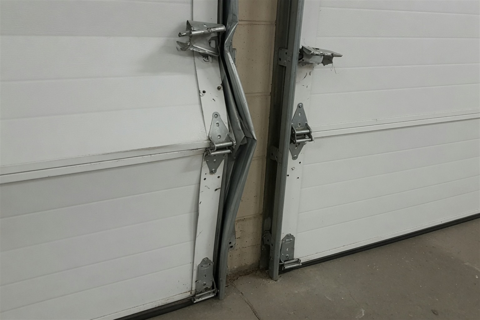 Damaged garage door with misaligned panels and bent track, showcasing the need for repair or replacement.